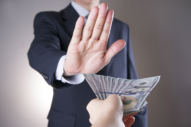 Person in a suit refusing a bribe by raising a hand while money is offered