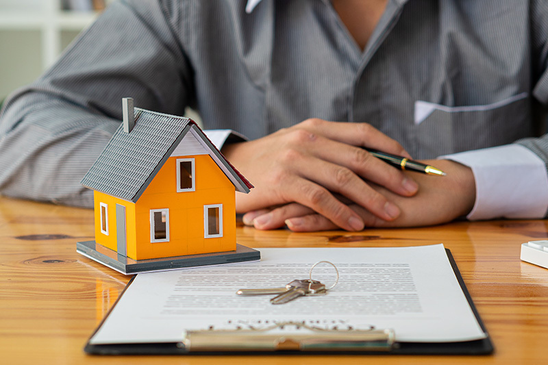 Person signing real estate contract with house model and keys on desk